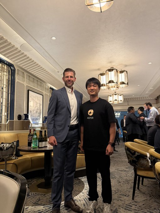 Two men pose together in an elegant lounge setting, one wearing a dark suit and the other in a black "ASTER" branded t-shirt, as they pose following a discussion on U.S. crypto regulatory developments and emerging workable paths for crypto derivatives and leverage trading.
