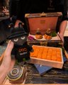 A small image showing an open box of baklava or similar Middle Eastern pastries alongside teacups on a table.