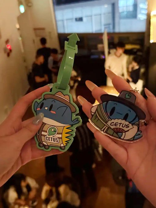 The image shows a person holding two keychains, one with a cartoon character design and another featuring a picture of a cat wearing a hat. The person's hands are visible as they hold these items. In the background, there are other people present in what appears to be an indoor setting, possibly at a party or gathering.

The post reads "Fifth day of June $SUI", which could indicate that it was posted on a social media platform like Instagram or Facebook. The image seems to be related to this post as the person holding the keychains is also part of the event being advertised.