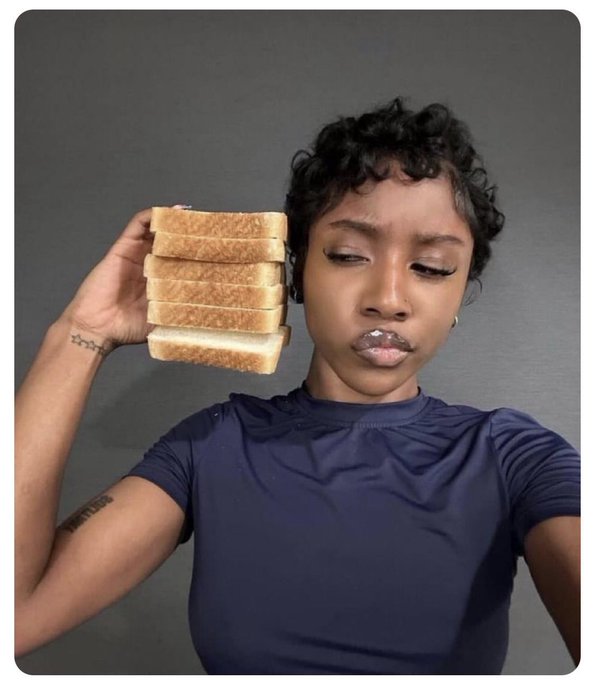 A person with short curly hair wearing a dark blue shirt holds a stack of sliced bread next to their face, with a smudge of white cream or food on their lips.