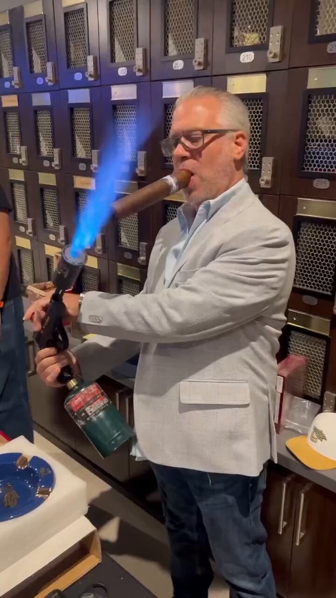 The image features a man dressed in a suit, standing next to a locker with a blue flame coming out of it. The man appears to be smoking something that looks like a pipe or a cigar, which has been lit using a lighter. He is wearing glasses and a jacket, giving him an air of sophistication. 

The post seems to be about Charles after the japanese bent the knee & getting one last juicy check before abandoning the chain for midnight. The image captures this moment with the man smoking something that resembles a pipe or cigar while standing next to a locker.