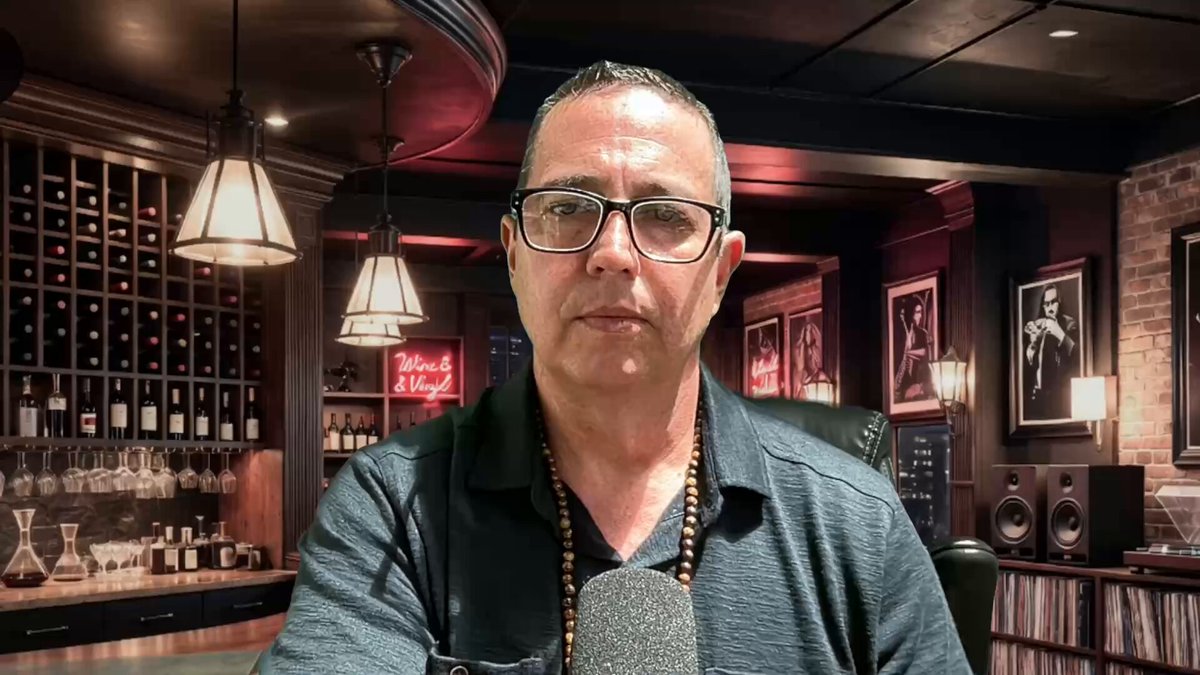 In the center of a dark bar, there's a man wearing glasses sitting down at a table with wine glasses on it. The background features several wine bottles lined up along the wall behind him, as well as other patrons enjoying their drinks in the room. At the bottom right corner of the image, you can see a post related to XRP and a cryptocurrency called Bitcoin Cash (BTC), possibly discussing or promoting the cryptocurrency.