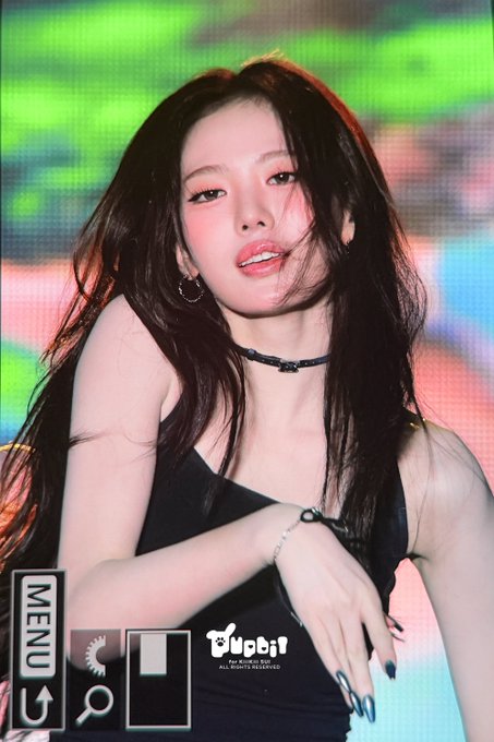 A young woman with long dark hair poses on a stage with green lighting, wearing a black top and choker, with 'MENU' and 'Young' text visible.