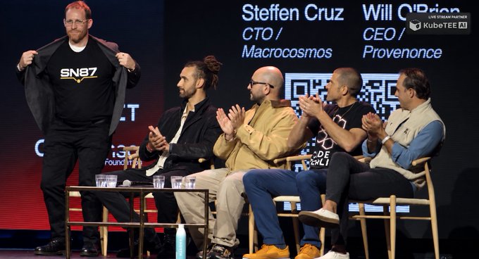 A panel of five men on stage at a KubeTEE AI event, with Steffen Cruz (CTO of Macrocosmos) and Will O'Brien (CEO of Provenance) visible on the backdrop, one man revealing a shirt reading 'sne7'.