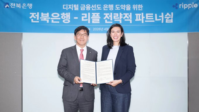 Two executives from Jeonbuk Bank and Ripple stand together holding an open signed agreement document in front of a banner displaying the partnership title in Korean, "전북은행-리플 전략적 파트너십" (Jeonbuk Bank-Ripple Strategic Partnership), dated April 2026, commemorating their newly announced collaboration to facilitate 24/7 cross-border payments with $XRP.