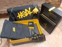 A yellow and black themed merchandise box set including a drawstring bag with 'HOOK' branding, a black zippered pouch, a water bottle, and other accessories on stone steps.