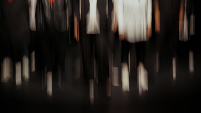 A blurry, dark photograph showing the legs and torsos of several people standing in what appears to be a dimly lit room.