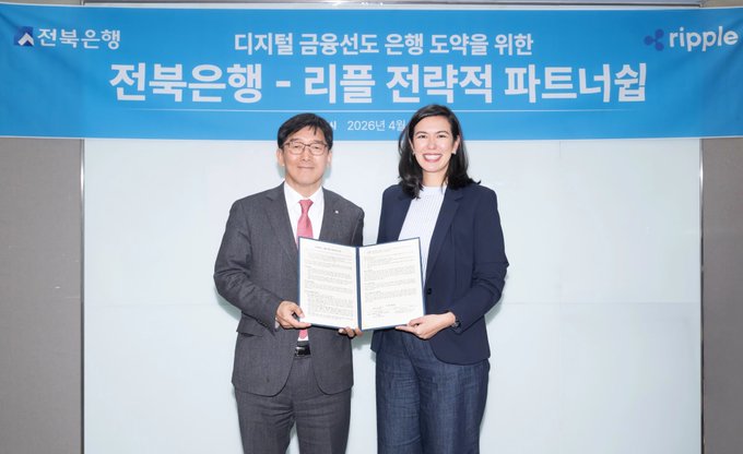 A man in a suit and a woman in a blazer hold a signed partnership agreement in front of a backdrop reading "전북은행 - 리플 전략적 파트너십" (Jeonbuk Bank - Ripple Strategic Partnership) with Ripple and Jeonbuk Bank logos, dated 2026. The image captures the signing ceremony marking Jeonbuk Bank as the first regional bank in Korea to adopt Ripple Payments for digital finance services.