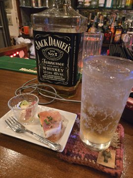 iced tea, a slice of pizza with green peppers and onions, and a Jack Daniel's whiskey bottle on a bar counter.