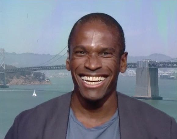 A smiling man stands in front of the San Francisco-Oakland Bay Bridge. The image accompanies news about BitMEX shutting down operations, with the bridge potentially symbolizing the closure or end of the cryptocurrency exchange's business.