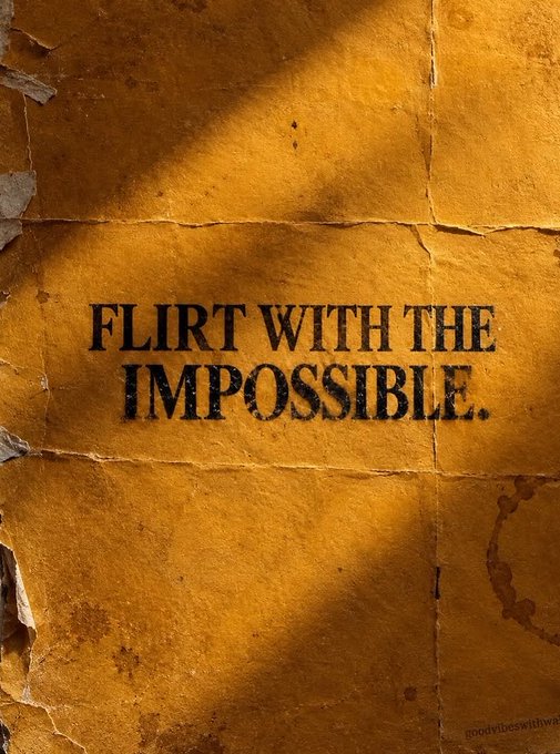 A motivational poster with the text 'FLIRT WITH THE IMPOSSIBLE.' stenciled in black on a textured, weathered yellow-orange wall, with 'goodvibeswithiwa' visible in the bottom right corner.