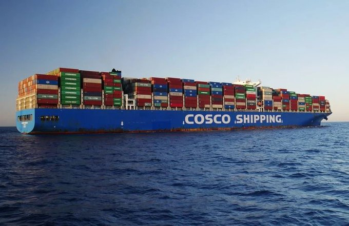 A massive COSCO SHIPPING blue container ship loaded with multicolored cargo containers sailing on the open ocean.