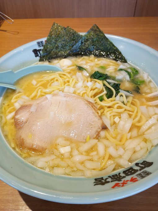 Photograph of a bowl of ramen with chashu pork, nori seaweed, spinach, and noodles in a light broth, with Japanese text on the bowl rim reading 'ラーメン我豚野郎'.