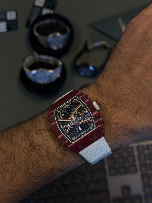 A bold red skeleton watch with a tonneau-shaped case and white strap sits on a hairy wrist, with luxury timepieces displayed on stands blurred in the background. The striking, unconventional design embodies the caption's "fuck around and find out" philosophy — a flashy, daring piece for someone willing to take style risks.