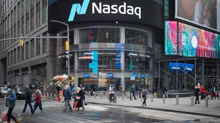 The image shows the Nasdaq MarketSite building in Times Square with its prominent "Nasdaq" signage displayed on the curved LED screen, as pedestrians walk along the sidewalk below. This iconic stock exchange headquarters serves as a fitting backdrop for the post announcing that Michael Saylor's MicroStrategy (MSTR) has surpassed Nasdaq's market cap, highlighting the growing financial influence of Bitcoin-focused companies over traditional stock market giants.