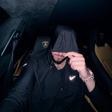 A man wearing a black hooded Nike jacket sits inside a luxury vehicle, partially concealing his face with the hood, with a Ferrari logo visible on the headrest behind him—suggesting a stylish, wealth-focused lifestyle that aligns with the post's promotion of Binance stock trading (#bStocks).