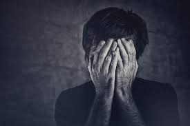 A black and white image of a person holding their head in their hands, conveying distress or anguish.