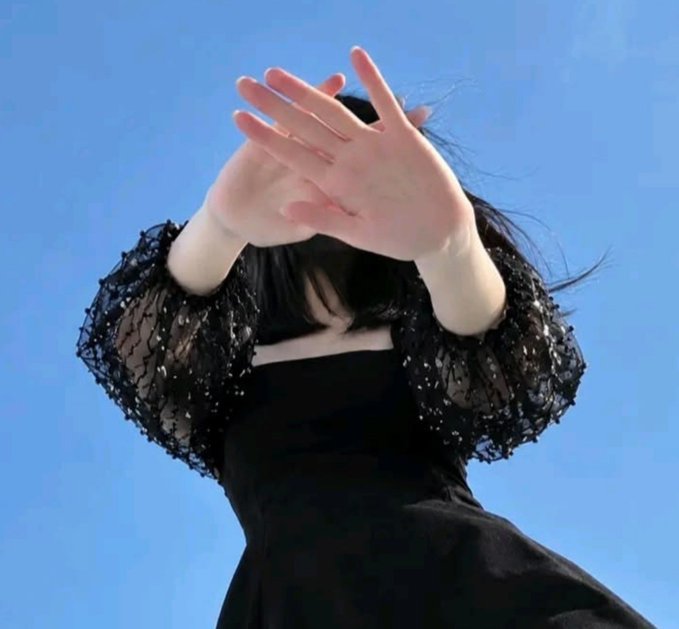 A young woman in a black lace-sleeve dress shields the sun with both hands, photographed from a low angle against a bright blue sky. The cheerful "gm guys:) Have a great day" greeting pairs nicely with the sunny, uplifting mood of the shot.