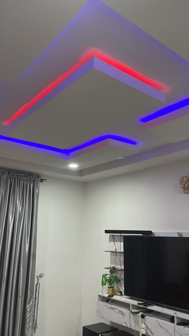 A modern living room ceiling design featuring geometric recessed panels illuminated with red and blue LED lighting, with a flat-screen TV mounted below.