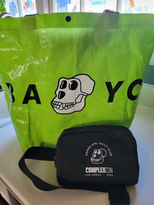 A green Bored Ape Yacht Club tote bag next to a black 'COMPLEXCON LAS VEGAS | 2025' branded fanny pack with the BAYC skull logo.