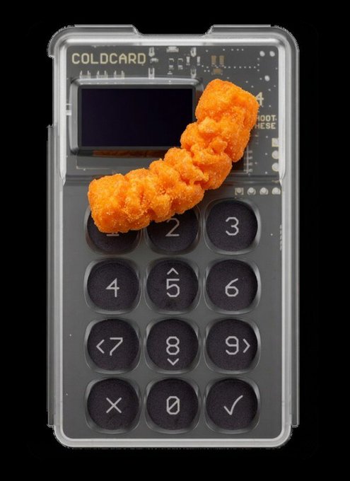 A COLDCARD hardware wallet device with a keypad, featuring a buffalo chicken tender placed on top of it, set against a black background.
