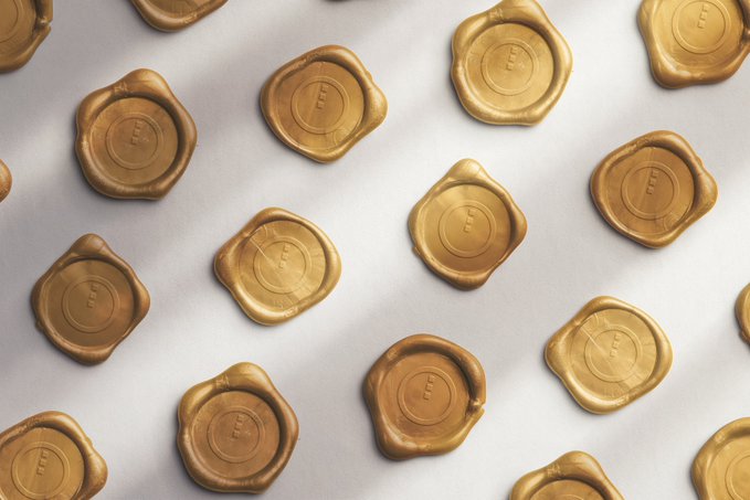 Overhead view of multiple gold wax seals stamped with an 'E' design scattered across a white surface.