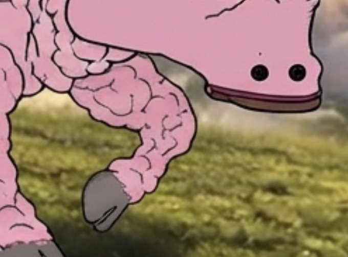 A close-up of a pink, cartoonish creature with bumpy, textured skin and simple dot eyes and mouth, standing on a grassy surface against a blurry background.