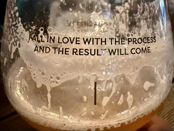 A close-up of a glass mug with condensation and bubbles, displaying the text 'FALL IN LOVE WITH THE PROCESS AND THE RESULT WILL COME' along with a fill line marker.