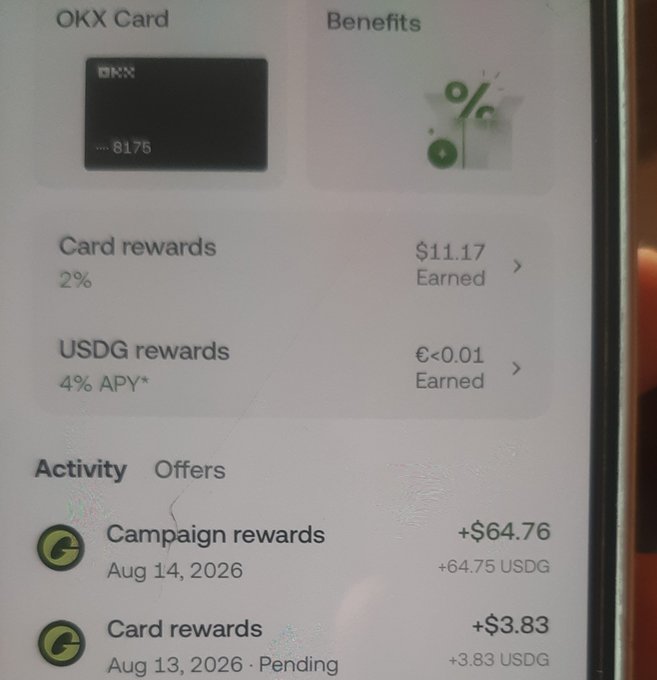 The image shows an OKX Card benefits screen displaying $11.17 in card rewards (2%) and USDG rewards (4% APY), along with recent activity including a campaign reward of +$64.76 (64.75 USDG) on Aug 14, 2026 and a pending card reward of +$3.83 (3.83 USDG) from Aug 13, 2026. This directly supports the post's excitement about receiving $64 in USDG campaign rewards from their OKX card, equating to over a million rupiah in value.
