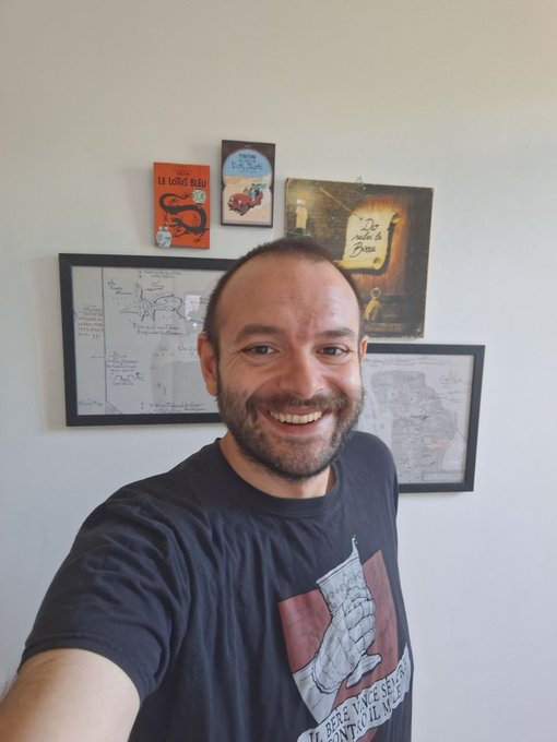 The image features a man wearing a black t-shirt with an interesting design, smiling at the camera while taking a selfie. The background of the photo includes several framed pictures hanging on a wall above him. The caption of the image reads "Beautiiies! Good morning!!! - Ryodan Pioneers Onboarding - Link in quoted post - MrGreenity Say Something at 1pm CET - Gaming on Immutable...as always - Connect with CT Fam".