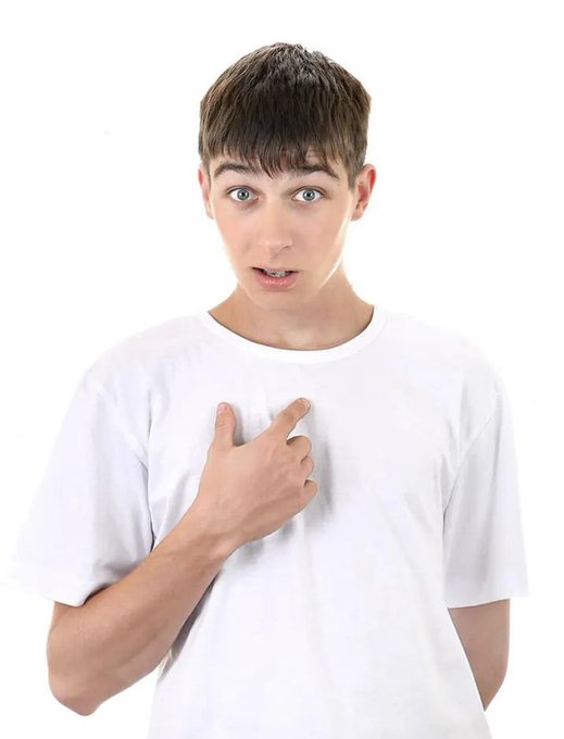 A young man with short brown hair wearing a white t-shirt, pointing at himself with a surprised expression.