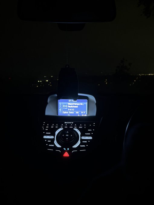 Inside a dark car, a Sony car stereo displays "BT-Audio" with the track "Nadi/Falena/Ar..." by "Soulsavers" playing at volume 14/10, with Options, Info, and 2h 11 elapsed time visible on the blue-lit screen. The dim, lonely interior paired with the timestamp suggests a long solo drive — fitting the contemplative "gulp" mood of a quiet moment alone on the road.
