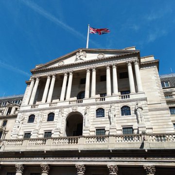 A large classical stone building with columns and a British flag flying on top, set against a blue sky.