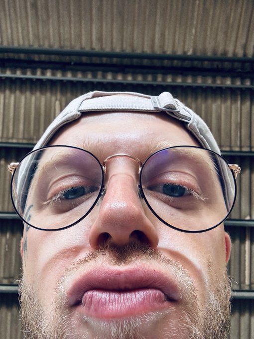 The image shows a man with glasses wearing a cap, looking at the camera and making an unpleasant facial expression for a close-up shot. The caption accompanying the image includes some weird and unusual terms such as "hyperliquid" or "zcash", which might be related to a recent online activity or slang in the conversation. Additionally, there are descriptions of people dressed poorly, possibly indicating that this is taking place at an underground club or other location with a more casual atmosphere.