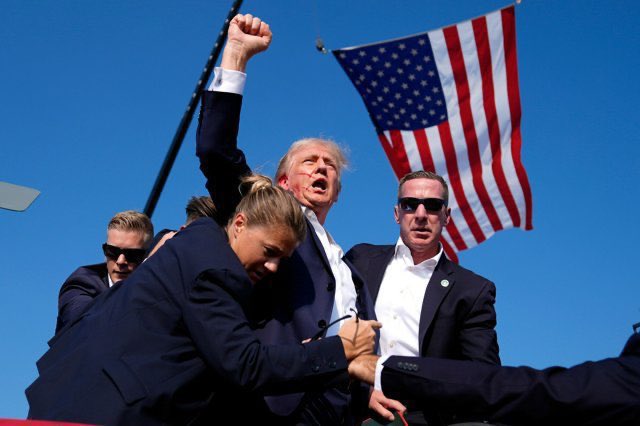 Donald Trump, with his fist raised and an American flag behind him, appears during an event. This image could relate to the post by referencing Trump's stance on economic matters like Bitcoin and its potential impact on the US dollar.