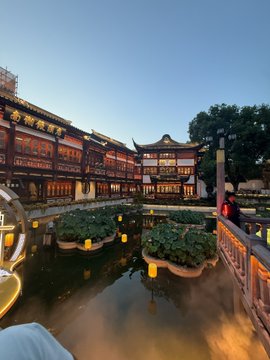 A traditional Chinese teahouse or cultural complex glows warmly beside a reflective pond at twilight, featuring ornate multi-tiered wooden architecture and floating lotus planters. The serene scene contrasts with the post's mention of taking a break from "workation," showcasing a likely leisure destination where the author is winding down amid an otherwise record-breaking sales week.