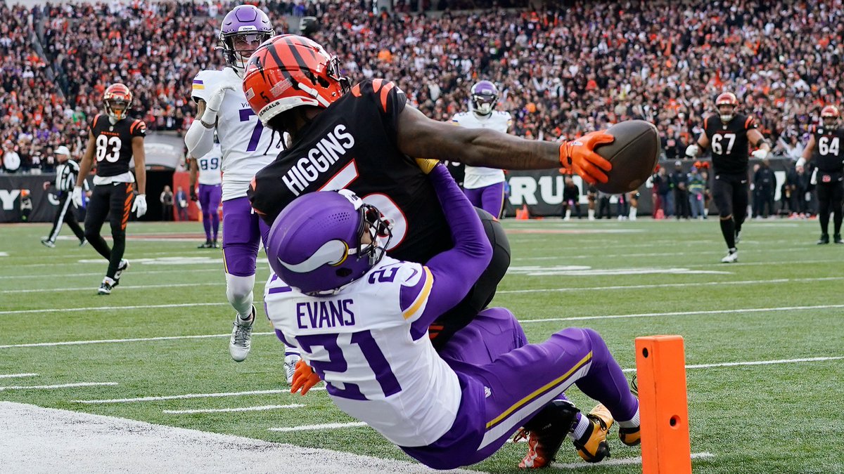 An NFL game action shot showing Cincinnati Bengals receiver #5 Higgins catching a touchdown pass in the end zone while falling backward over Minnesota Vikings defender #21 Evans, with the pylon visible.