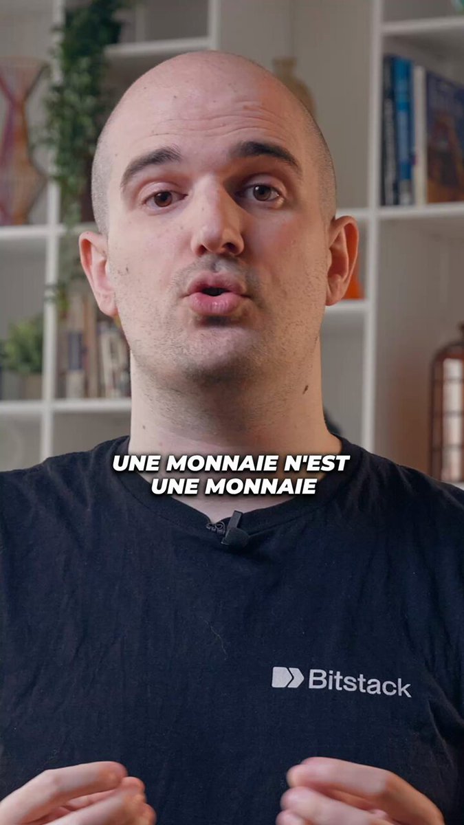 The image features an adult male wearing a black t-shirt with white text that says "Bitcoin est-il en train de devenir une monnaie mondiale ? Dans cet extrait, Alexandre Stachtchenko explore une question simple : si vous deviez partir n’importe où dans le monde avec un seul actif, lequel choisiriez-vous ?". The man is standing in front of a bookshelf filled with various items.

The image also contains the text "Un une monnaie en train de devenir une monnaie mondiale ? Dans cet extrait, Alexandre Stachtchenko explore une question simple : si vous deviez partir n’importe où dans le monde avec un seul actif, lequel choisriez-vous ?". This text is written in French and is located at the bottom of the image.