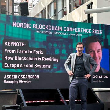 The image features a man standing next to a large billboard, which displays information about an event called the Nordic Blockchain Conference. The event appears to be taking place in Stockholm, as indicated by the date "26th May - 27th May" on the poster. The man is posing for the picture and seems to be interested in attending or participating in this conference.