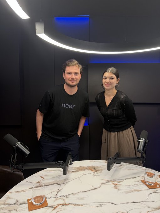Two people pose together in a podcast studio setup with a marble table, professional microphones, and curved overhead lighting. The man wears a black "near" t-shirt, visually connecting to the post about meeting in person to discuss @near_intents and the NEAR ecosystem for a podcast episode.