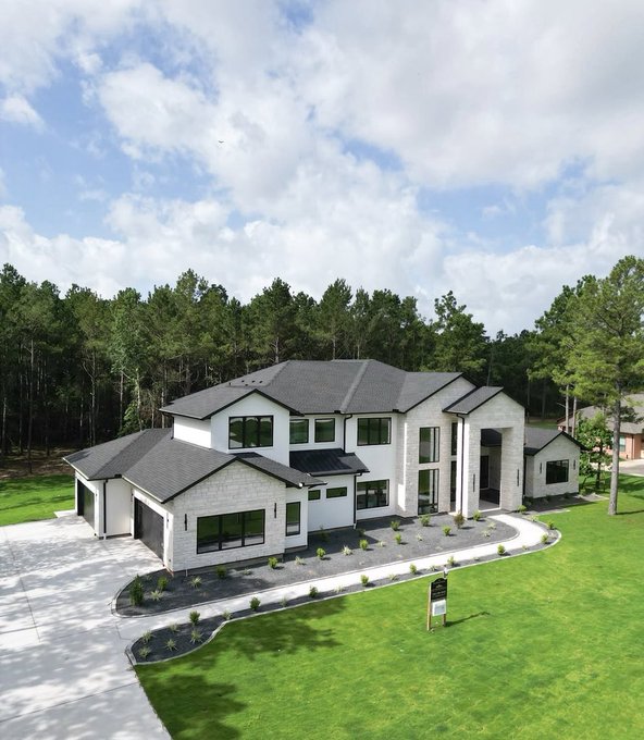 A luxurious modern white home sits nestled among lush green lawns and dense trees, with a real estate sign in the front yard suggesting it's for sale—visually symbolizing the dream of homeownership that the post suggests will be made possible through memecoin profits by year's end.