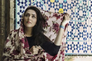 A young woman with long dark hair, wearing a black top and a floral scarf, stands against a colorful geometric tile wall, gazing thoughtfully to the side. The image accompanies a post thanking the XRP community for their support on an XRP NFT collection, likely serving as a promotional visual for the creator.