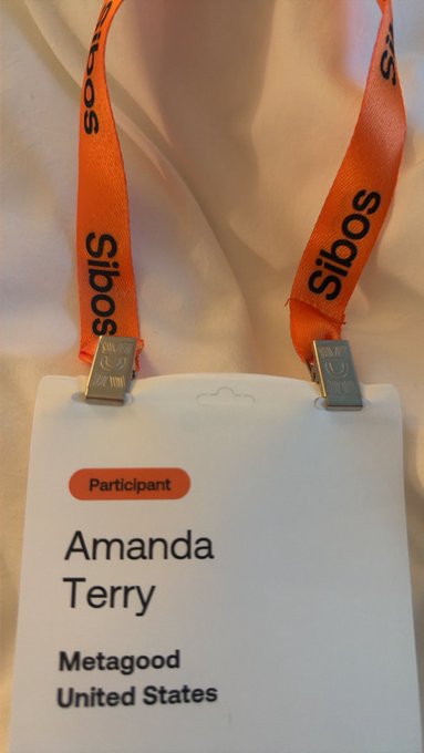 A close-up of a 'Participant' badge for Amanda Terry from Metagood in the United States, hanging from an orange 'Sibos' lanyard.