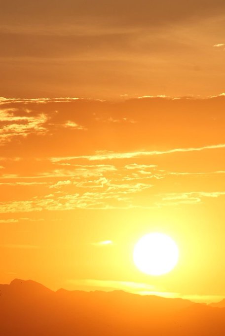 A vibrant orange sunset with the sun glowing brightly over distant mountains, casting warm hues across the sky.