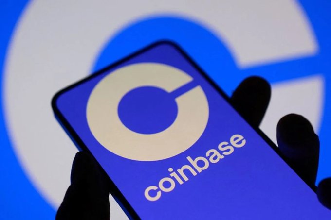A smartphone displays the Coinbase logo (blue circle with a 'C') with 'coinbase' text, set against a larger background showing the same logo.
