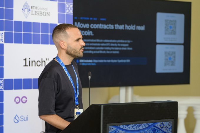 A man with a shaved head and beard speaking at a podium during ETHGlobal Lisbon, with a slide behind him titled 'Move contracts that hold real coin.' showing text about 1inch.