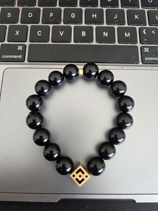 A black beaded bracelet with a gold geometric charm rests on the trackpad of a MacBook laptop.