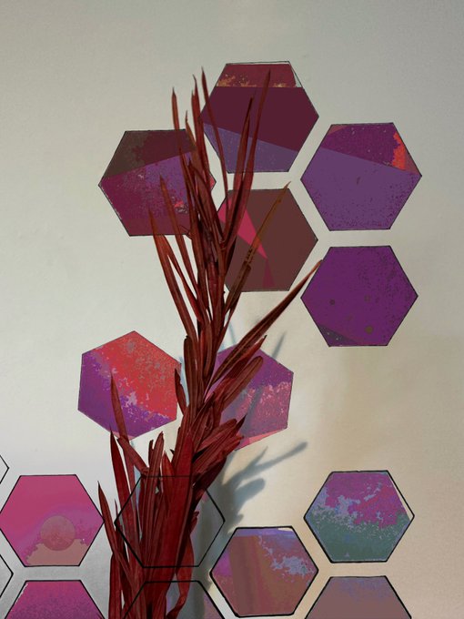 A decorative arrangement of purple and magenta hexagonal mirrored wall tiles with dried reddish plant stems placed in front of them.