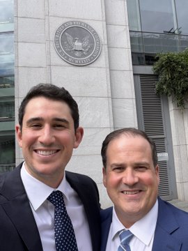 Two smiling men in suits pose for a selfie in front of the U.S. Securities and Exchange Commission (SEC) building in Washington, D.C., symbolizing the post's theme of productive engagement with the SEC on Reg Crypto and investor protection.