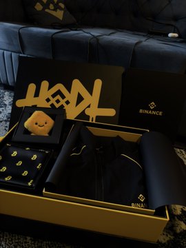 A black and gold Binance-branded merchandise gift box containing a t-shirt, baseball cap, and other accessories with the Binance logo and 'BNB' designs.